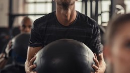 Man carrying weighted exercise ball in group gym session